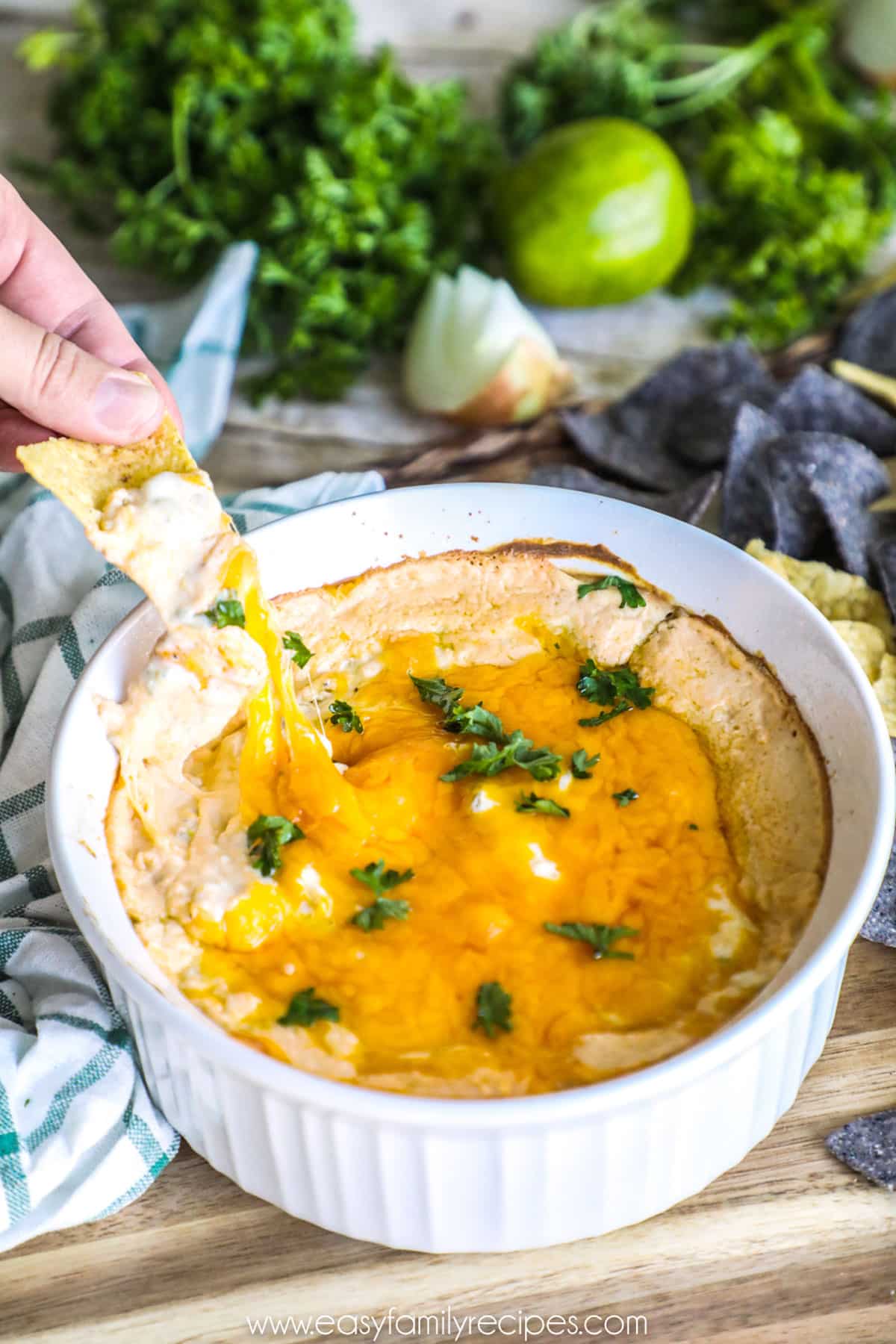 Green chile dip in a baking dish with a chip being dipped into it.