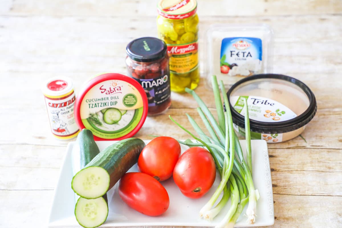 Ingredients needs for the Greek Layer Dip - hummus, tzatziki, greek seasoning, cucumbers, tomatoes, feta, olives and pepperoncini's 