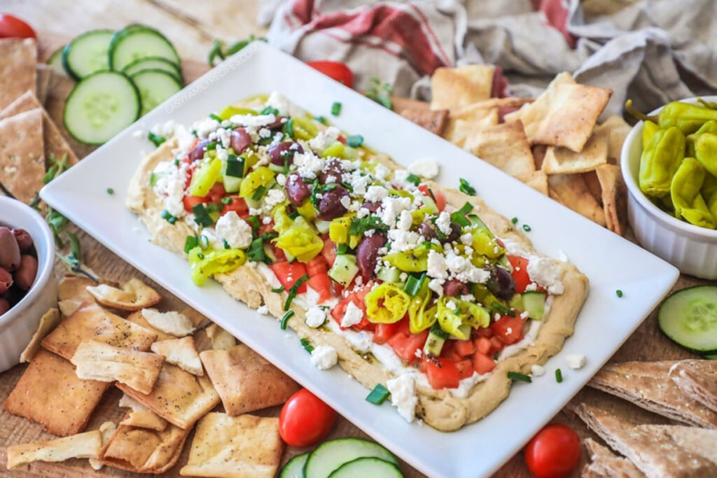 Greek layer dip served as an appetizer on a platter with pita chips and vegetables.