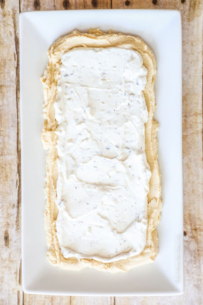 How to make Layered Greek Dip Step 1: Spread on hummus and tzatiki.