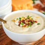 Creamy Cauliflower soup made in the Instant Pot then served in a bowl topped with sour cream, bacon, green onions, and cheese