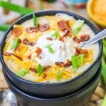 Loaded baked potato soup made in a crockpot and served in a bowl topped with cheese sour cream, bacon, and chives