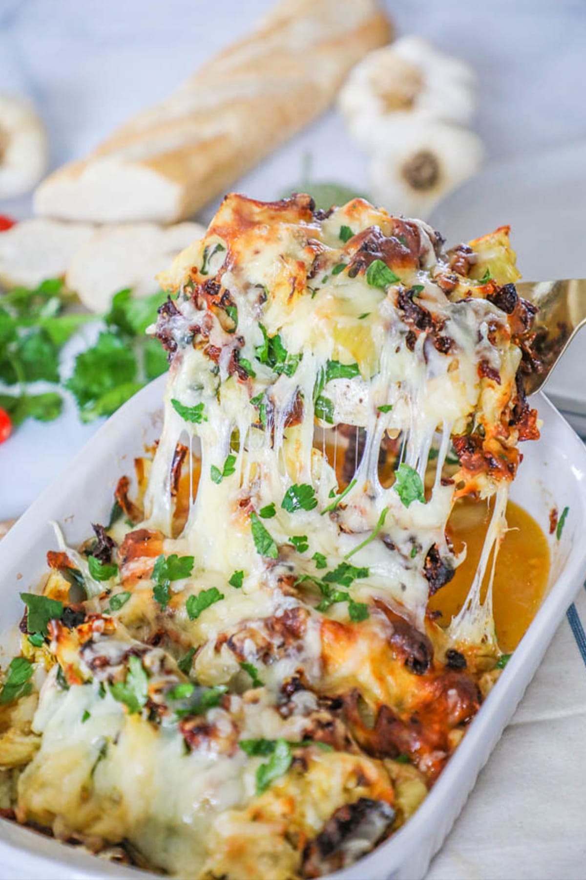 A gold spatula in a white casserole dish that is filled with baked Tuscan Garlic Chicken.