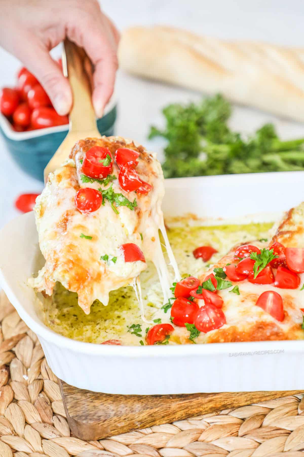 Lifting cheesy pesto chicken breast out of casserole dish.