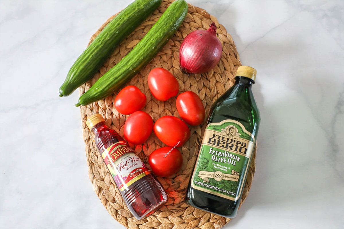 Ingredients to make cucumber tomato salad - cucumbers, tomatoes, onion, olive oil and red wine vinegar