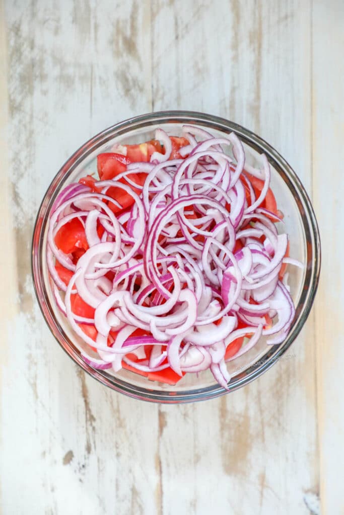 Step 3 - Finely slice the red onion into half moons and combine all of the vegetables in a large bowl.