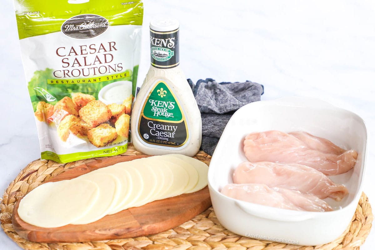 Ingredients for making caesar chicken including chicken breast, kens caesar dressing, provolone cheese, and croutons.