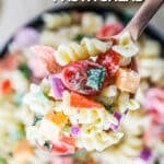 A spoon scooping out Rotini Salad with pepperoni, cheeses, and veggies in a bowl