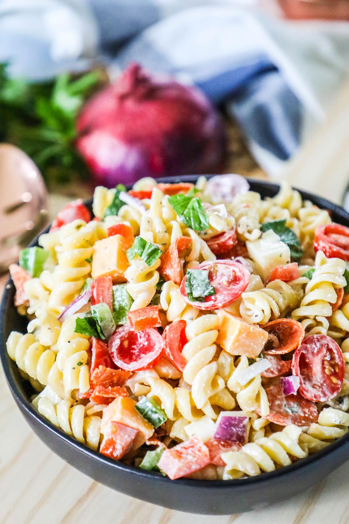 A black bowl with Rotini Salad with pepperoni, cheeses, and veggies in a bowl