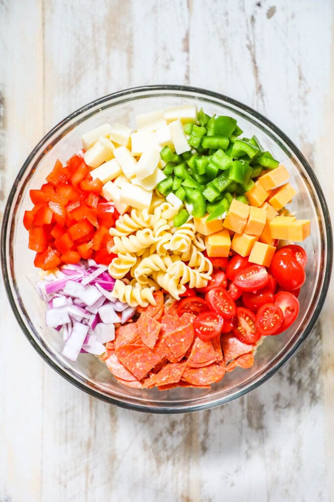 Step by step recipe for Rotini Pasta Salad. Step 2: Prep remaining ingredients, then add the cheese, peppers, tomatoes, onion, pepperoni, and basil to the pasta.