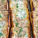 Buttery Garlic Bread with crispy brown edges on a baking sheet garnished with parsley