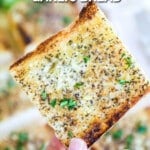 Hand holding up a slice of homemade garlic bread that is buttery and delicious.