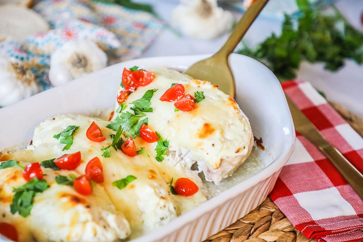 Creamy Baked garlic parmesan chicken being lifted from casserole dish to serve for an easy dinner.