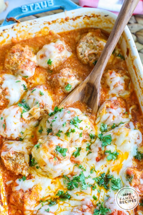 Parmesan Meatballs covered in cheese in Casserole dish with a spoon