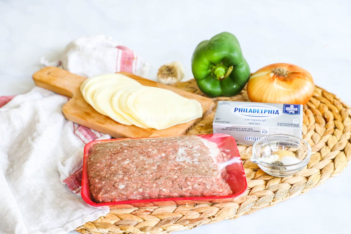 Ingredients for philly cheesesteak casserole including ground beef, cream cheese, bell pepper, onion, provolone cheese and spices