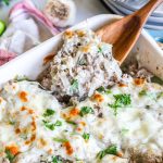 Philly Cheesesteak Casserole in a baking dish and scooping out a big cheesy serving.