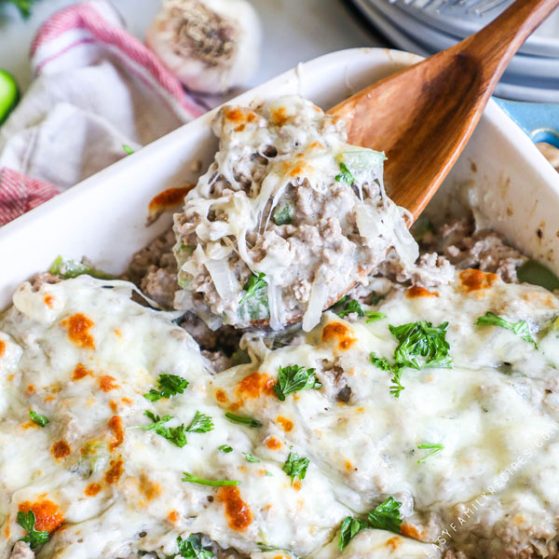 Philly Cheesesteak Casserole in einer Auflaufform und schöpfen eine große käsige Portion aus.