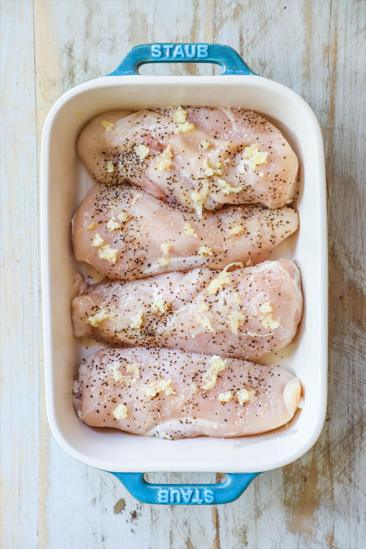 Step 1 of baked Hawaiian chicken. Chicken is in a white dish with seasonings.