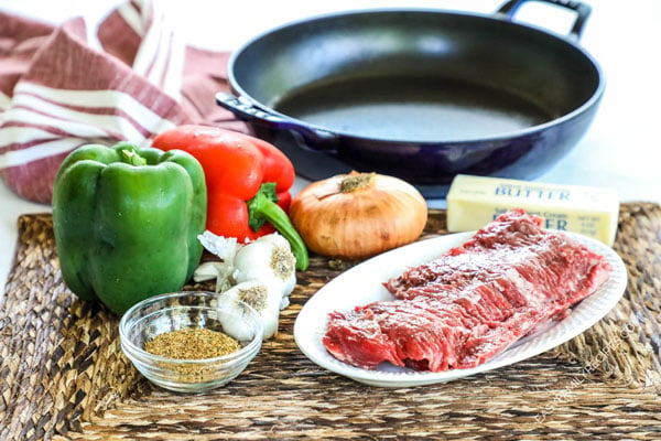 Ingredients for making steak fajitas including skirt steak, bell peppers, onion, and steak fajita marinade