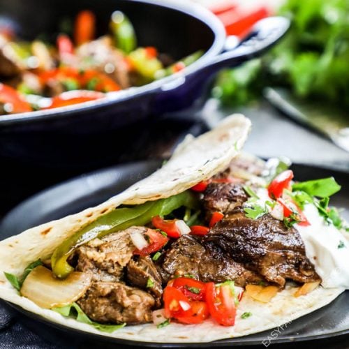 Steak Fajitas Recipe placed in a tortilla and topped with pico de gallo and sour cream