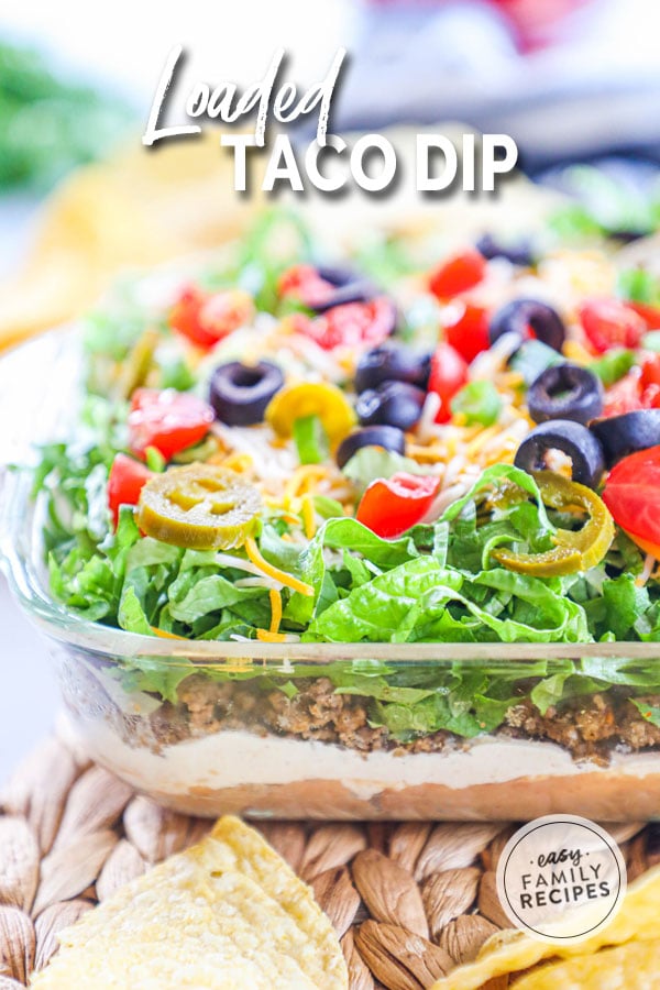 Taco dip from the side so you can see layers of beans, meat, cream cheese, sour cream, lettuce and tomatoes