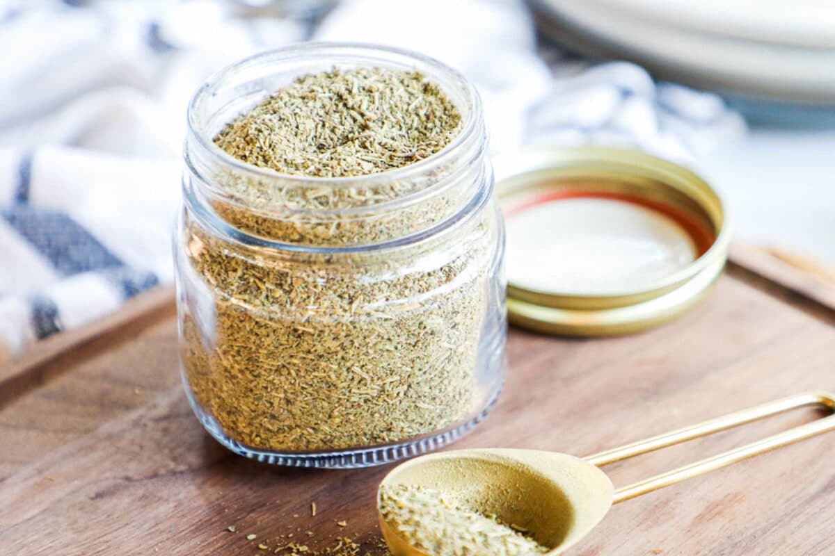 Homemade Italian Seasoning in a glass jar with a measuring spoon next to it