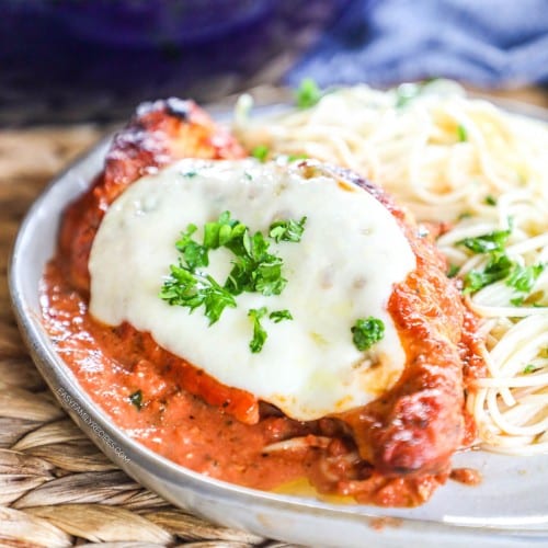 Chicken Mozzarella made in a skillet and plated in creamy tomato sauce topped with basil next to pasta