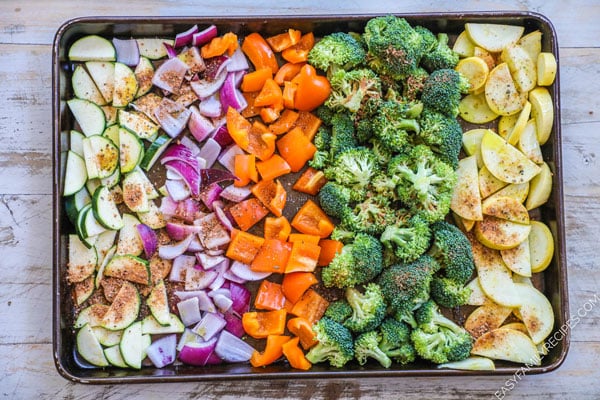 Ingredients for roasted veggies on a cookie sheet including zucchini, squash, broccoli, onion, bell pepper, and cajun seasoning.