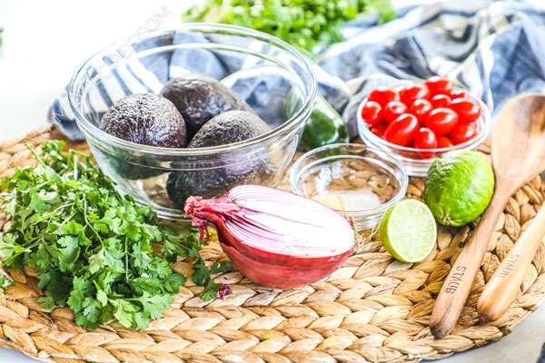 Guacamole ingredients including avocado, onion, lime, tomato, cilantro, garlic and salt