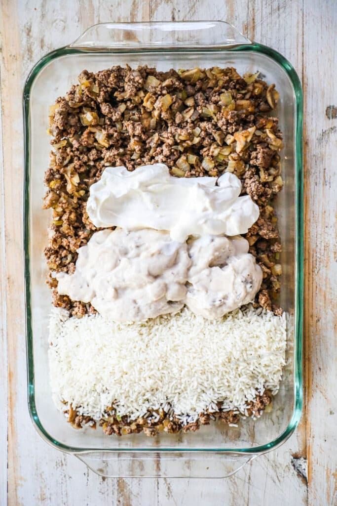 Second step process image showing how to mix in mushroom soup, sour cream, rice, and beef broth on top of the beef mixture. 