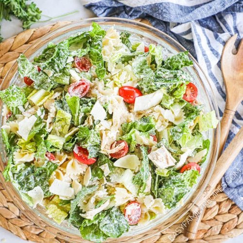 Overhead view of a big bowl of chicken caesar pasta salad with serving spoons next to it on a napkin