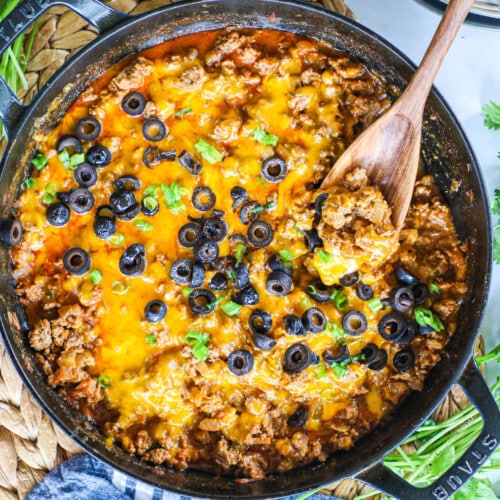 Cheesy ground beef skillet enchiladas topped with cheddar cheese, black olives, and green onions.