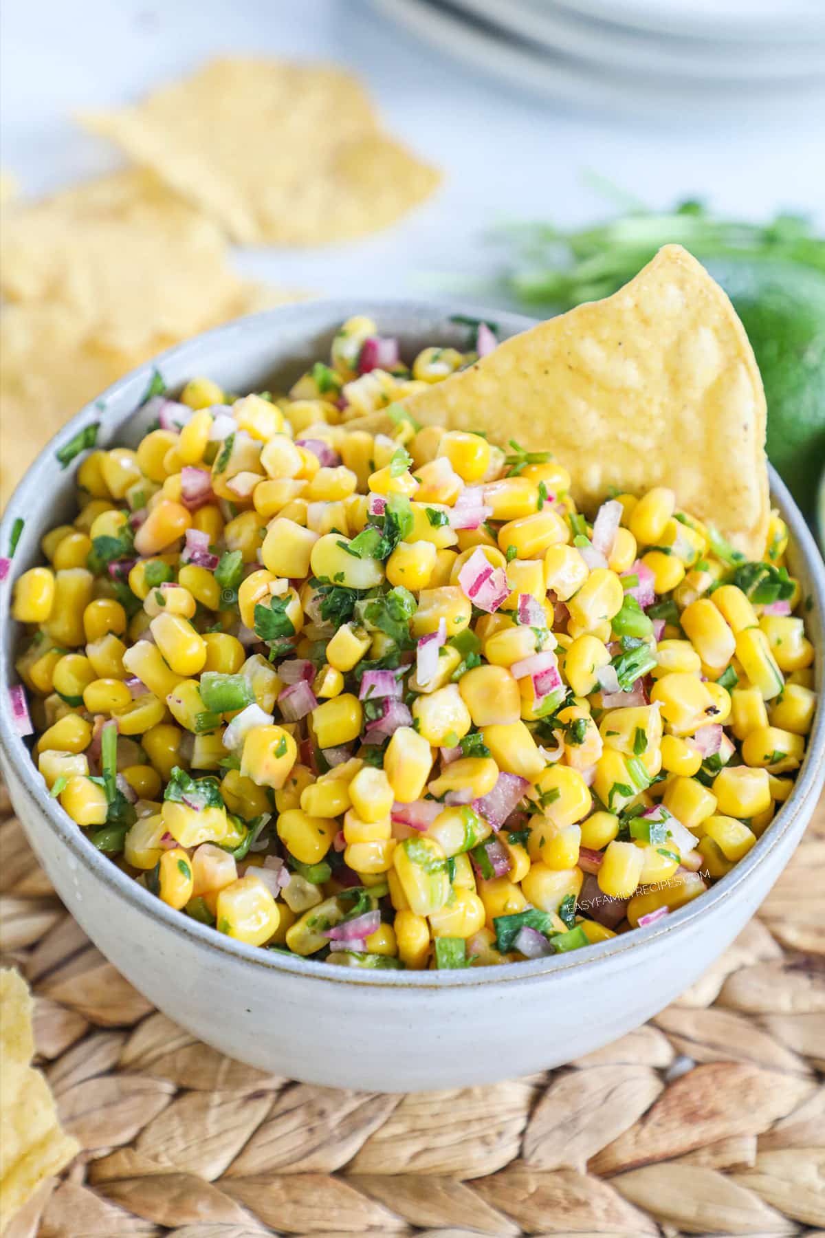 A white bowl of corn salsa and a chip