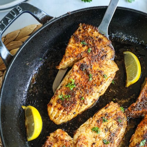 Blackened fish cooked in a cast iron skillet and garnished with lemon wedges and parsley