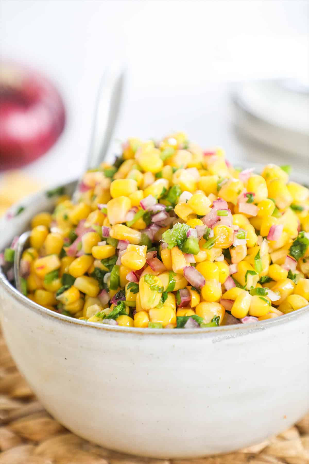 A white bowl of corn salsa and a spoon