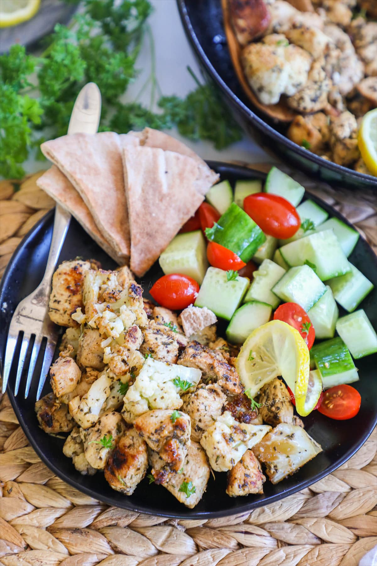 Overhead view of a plate with sautéed greek chicken and cauliflower flavored with greek seasoning and lemon with a side of cucumber salad.