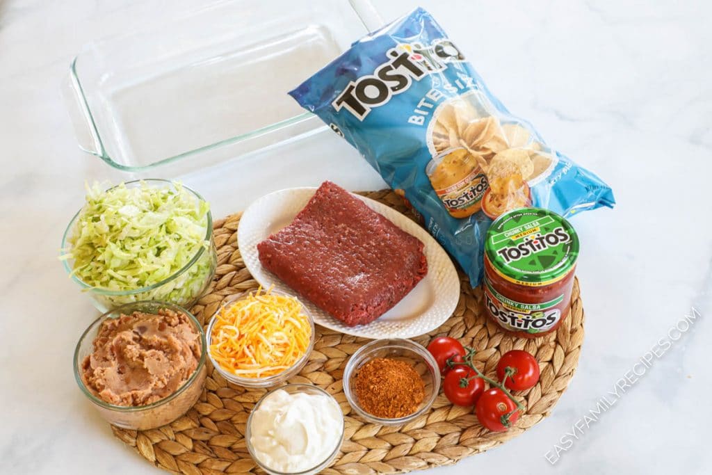 Taco Casserole ingredients including - ground beef, beans, cheese, taco seasoning, lettuce, tomato, salsa and chips