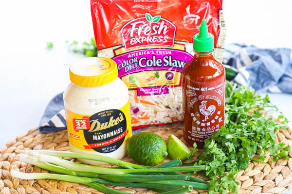 Ingredients for spicy asian coleslaw including cabbage or coleslaw mix, mayonnaise, lime juice, sriracha, green onions, cilantro