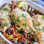 Serving dish with greek chicken with red onion, pepperoncini peppers, roasted red peppers, spinach and olives