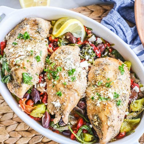 Serving dish with greek chicken with red onion, pepperoncini peppers, roasted red peppers, spinach and olives