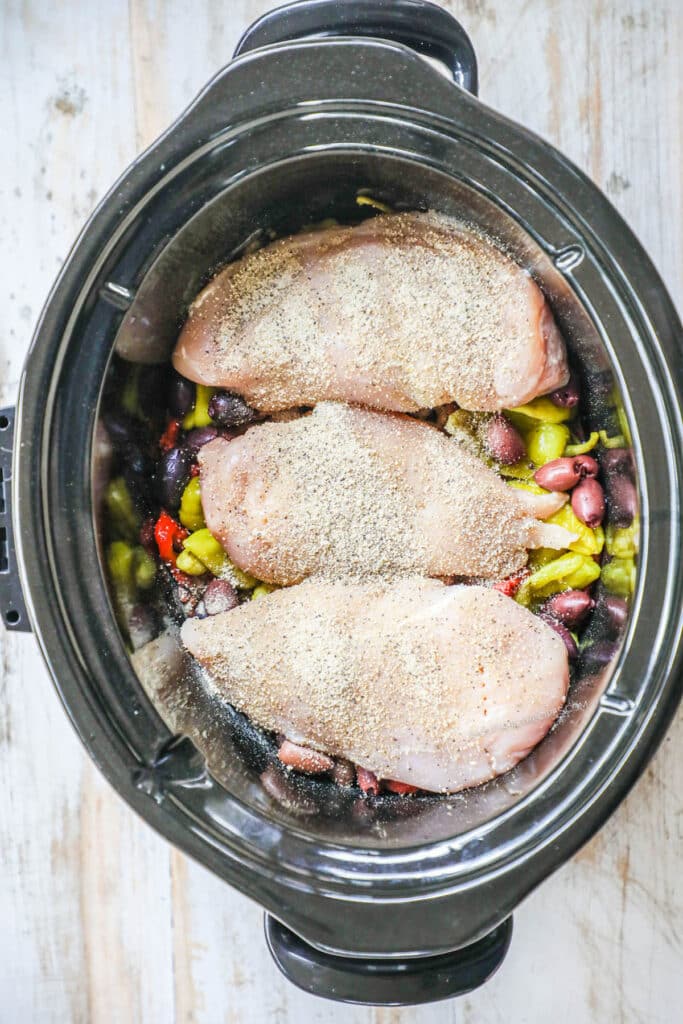 Step 1 Crockpot Greek Chicken Recipe - Drain the red bell pepper strips, peperoncini peppers, and olives and layer them in the crock pot.
Season the chicken on both side and lay them on top of the pepper mixture. Cover with onions and garlic.