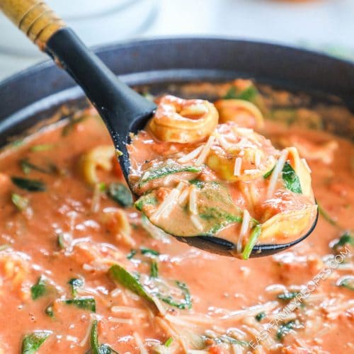 Lifting a big scoop of tomato tortellini soup from the pot on the stove top