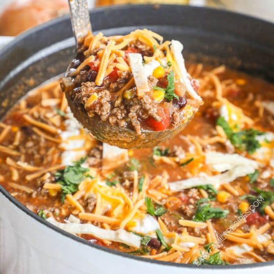 Ladle serving ground beef enchilada soup with sour cream and cheese