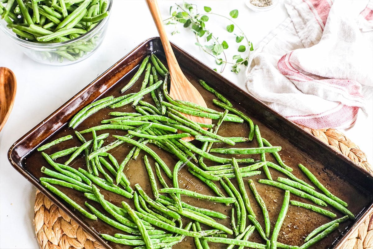 green beans on a sheet pan and a wooden spoon underneath to serve green beans