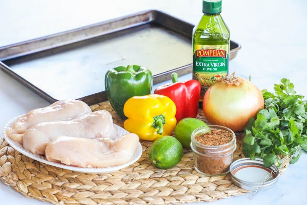 Ingredients for making baked sheet pan chicken fajitas including chicken breast, bell pepper, onion, lime, fajita seasoning, oil