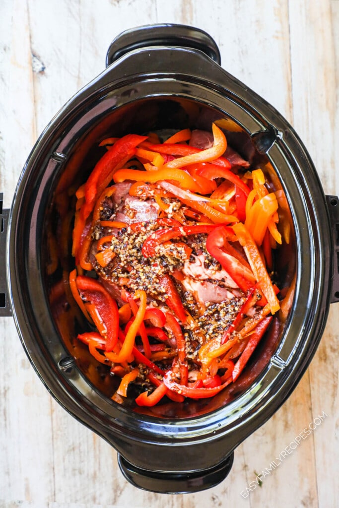 How to make thai pork in crockpot step 2: cover pork with sliced red bell pepper, sauces, and seasonings.