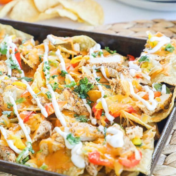 Cheesy Chicken Fajita Nachos baked on a sheet pan and drizzled with sour cream.