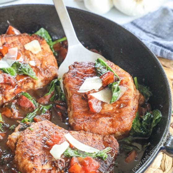 Boneless pork chops cooked tuscan style in a skillet garnished with tomatoes and parmesan