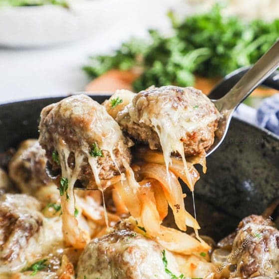 Lifting cheesy meatballs with sauteed onions from skillet with spoon