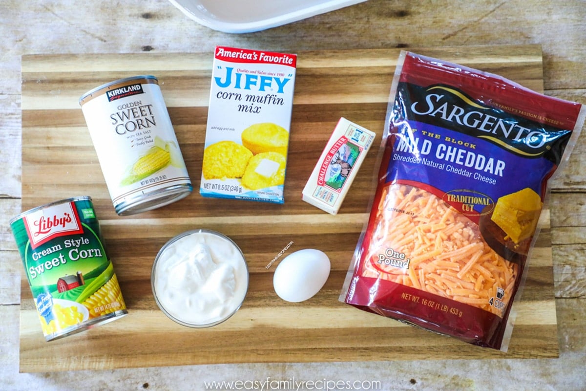 Ingredients for making Jiffy Corn Casserole including Jiffy cornbread mix, cream corn, canned corn, cheddar cheese, sour cream, eggs, and butter.